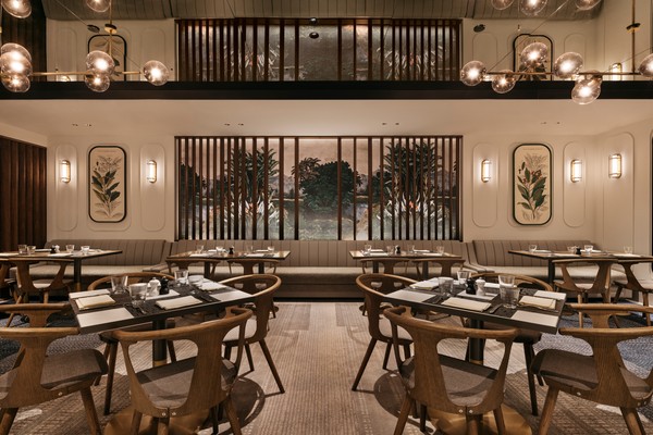 An elegant dining room with neatly arranged tables and chairs, warm lighting, framed botanical illustrations, and a window overlooking trees.