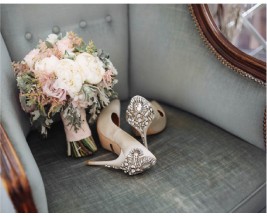 A pair of embellished high-heeled shoes rests beside a bouquet of flowers on a vehicle seat, suggesting a special occasion like a wedding.