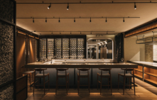 Wine bar with stools, warm lighting, and wall-mounted wine shelves in a contemporary setting.