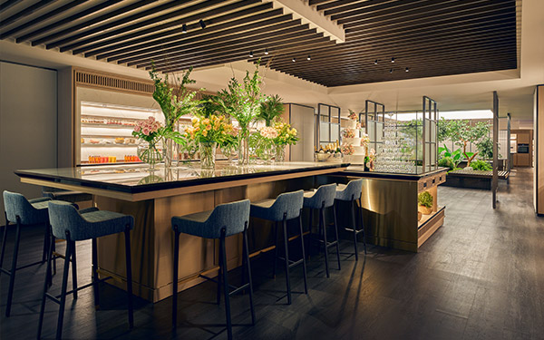 A modern bar with stools and vibrant flowers is set in an elegant room with wood flooring and warm lighting.