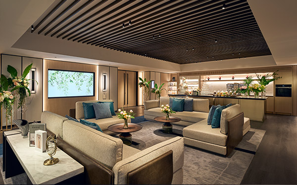 Elegant lounge area with plush sofas, decorative pillows, ambient lighting, framed by a sleek bar and slatted ceiling, invoking a cozy yet luxurious atmosphere.