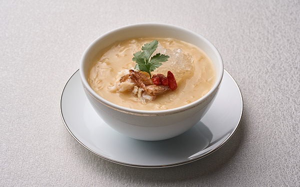A bowl of creamy soup garnished with herbs and chili, served on a saucer, set against a neutral-toned background.
