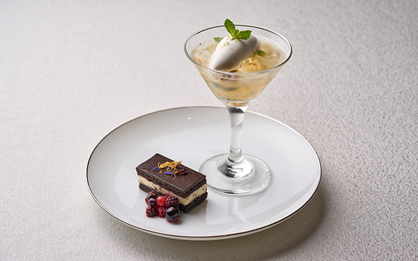 A dessert ensemble on a white plate features a layered chocolate cake with berries and a martini glass containing ice cream and fruit, presented on a textured surface.